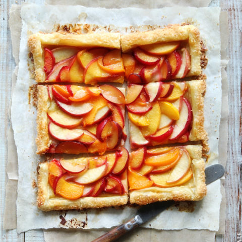 Summer fruit tart cut into six pieces on a cutting board with a knife.