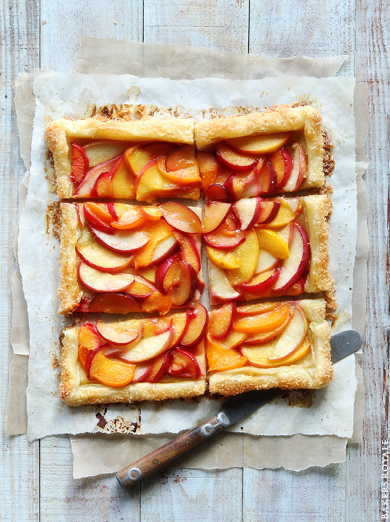 Summer fruit tart cut into six pieces on a cutting board with a knife.